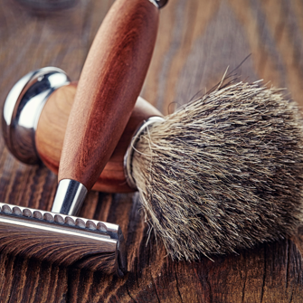 A shaving brush and safety razor on an oak counter